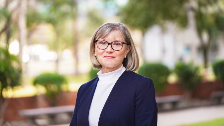Sarah Felknor, DrPH, pictured in front of greenery and brick wall in background.