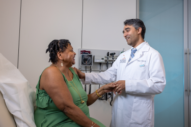 Doctor in white coat holding hands with a seated patient during a consultation in a medical office.