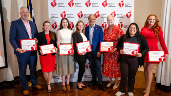 Eight adults posing for a photo holding certificates in front of an American Heart Association backdrop.