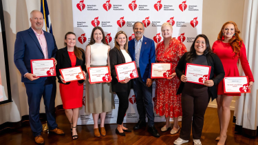Eight adults posing for a photo holding certificates in front of an American Heart Association backdrop.